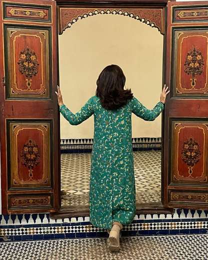 Viajera abriendo unas puertas de madera pintada hacia un patio alicatado en Marrakech